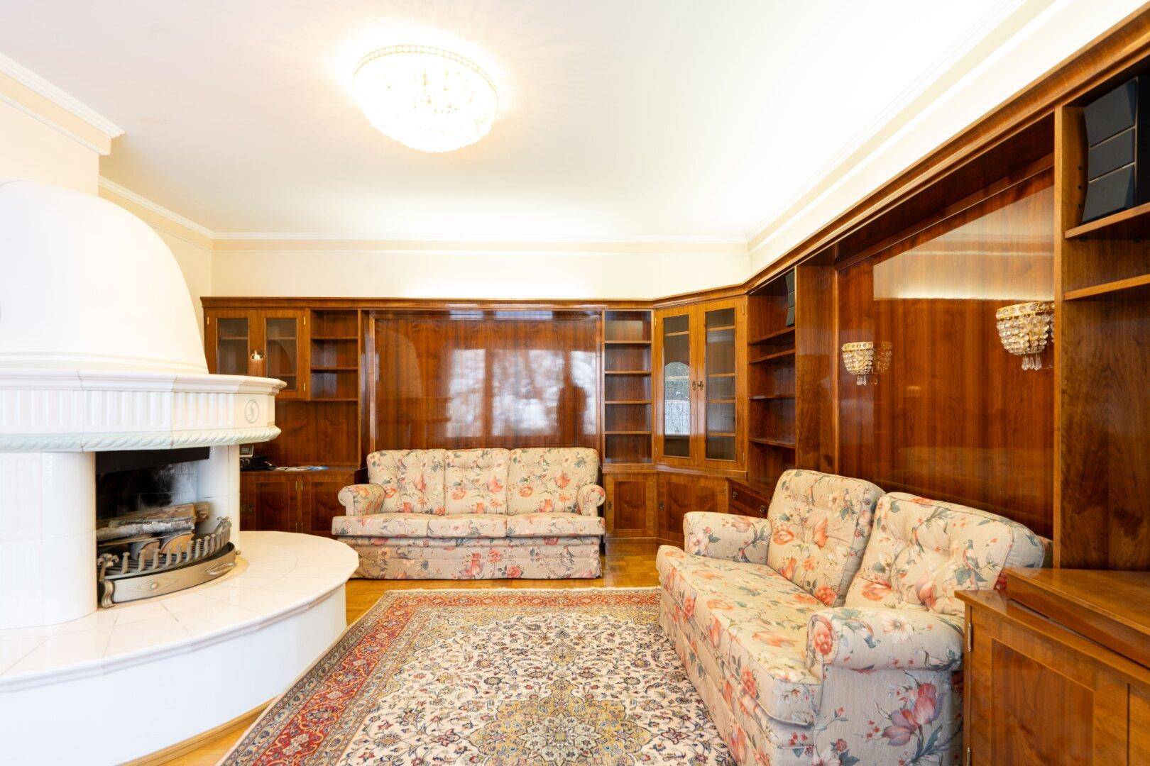 Gemütliches Wohnzimmer mit Kamin, Einbauschränken und floralen Sofas, die zum Entspannen einladen.