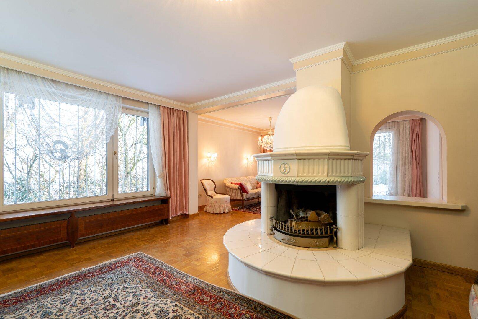 Geräumiges Wohnzimmer mit großem Kamin, Parkettboden und Blick nach draußen, ideal für kalte Tage.