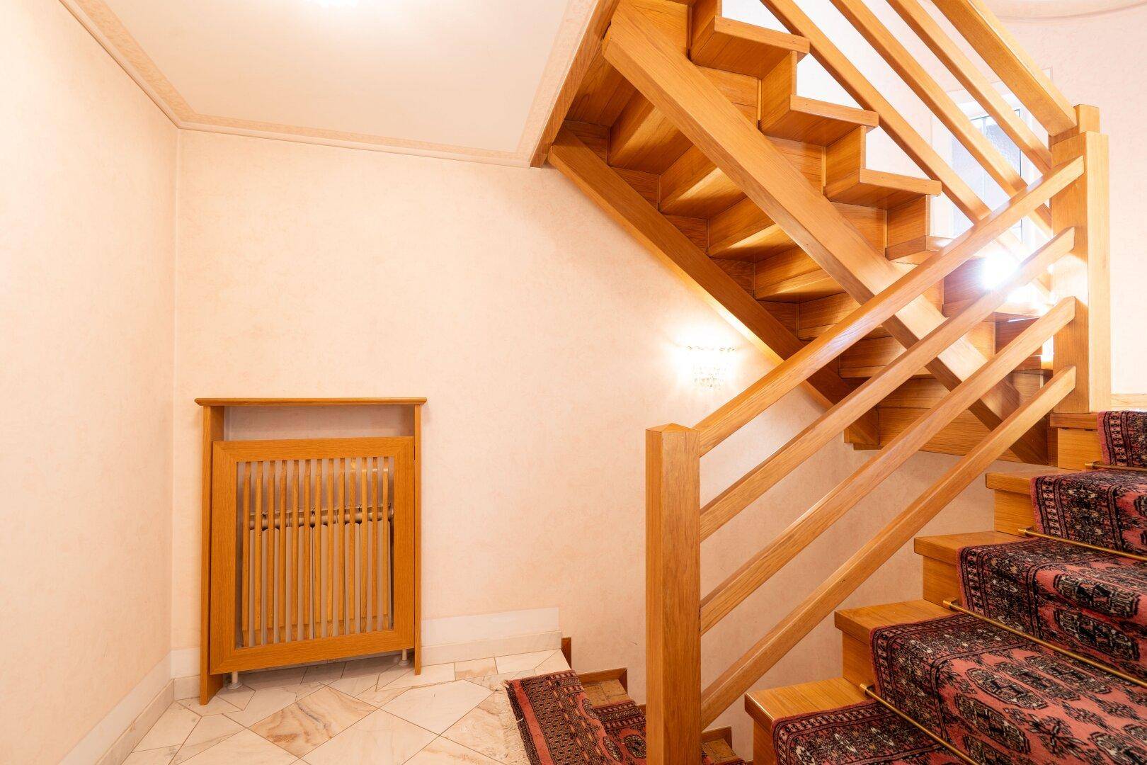Elegante Holztreppe mit Teppichläufer und hellem Treppenhaus, das die Stockwerke verbindet.