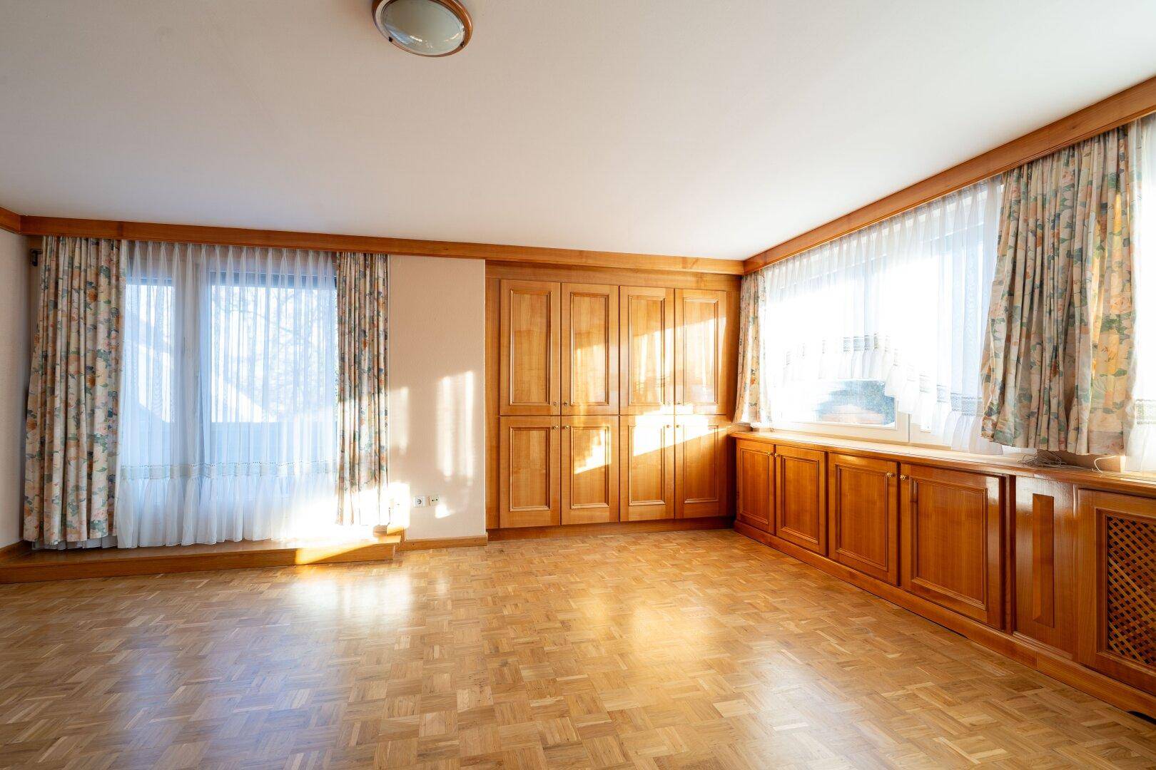 Helles Zimmer mit vielen Holzschränken und Parkettboden, das eine warme und einladende Atmosphäre schafft.