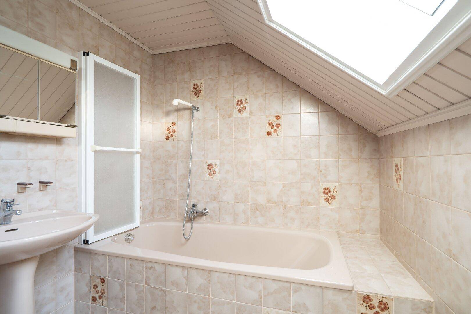 Badezimmer mit Badewanne, Dachfenster und gemusterten Fliesen, die eine helle und funktionale Umgebung schaffen.