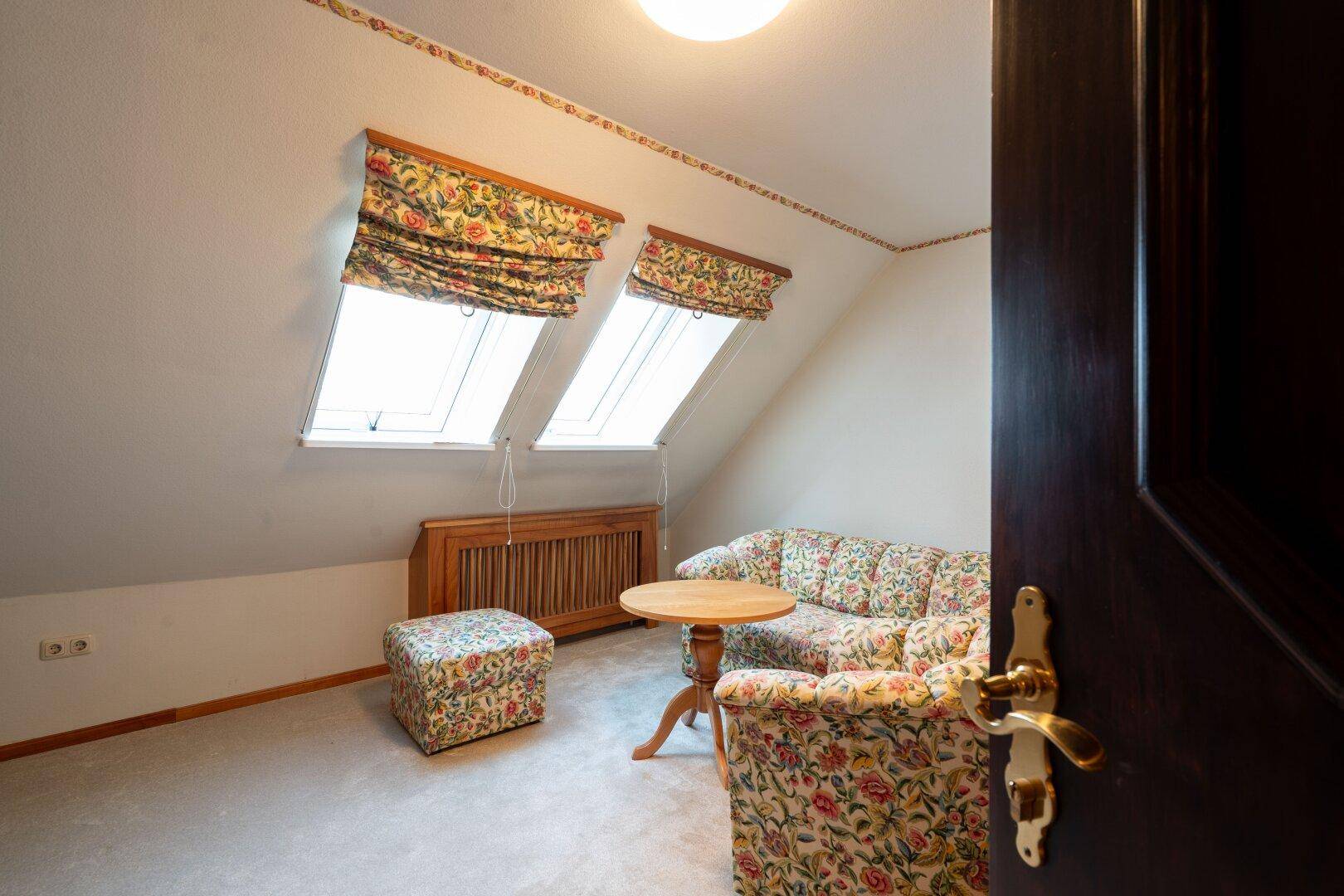 Gemütliches Dachzimmer mit Sofa, Couchtisch und Dachfenstern, die viel Tageslicht hereinlassen.