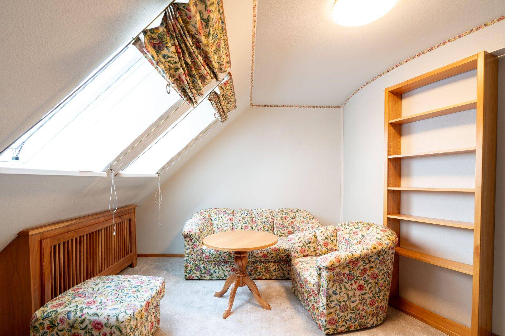 Helles Dachzimmer mit Sofa, Bücherregal und Dachfenstern, die eine angenehme Leseatmosphäre schaffen.