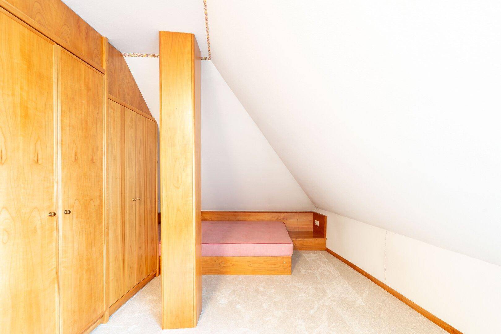 Schlafzimmer im Dachgeschoss mit Einbaubett, Holzschränken und Teppichboden, das eine gemütliche Nische schafft.