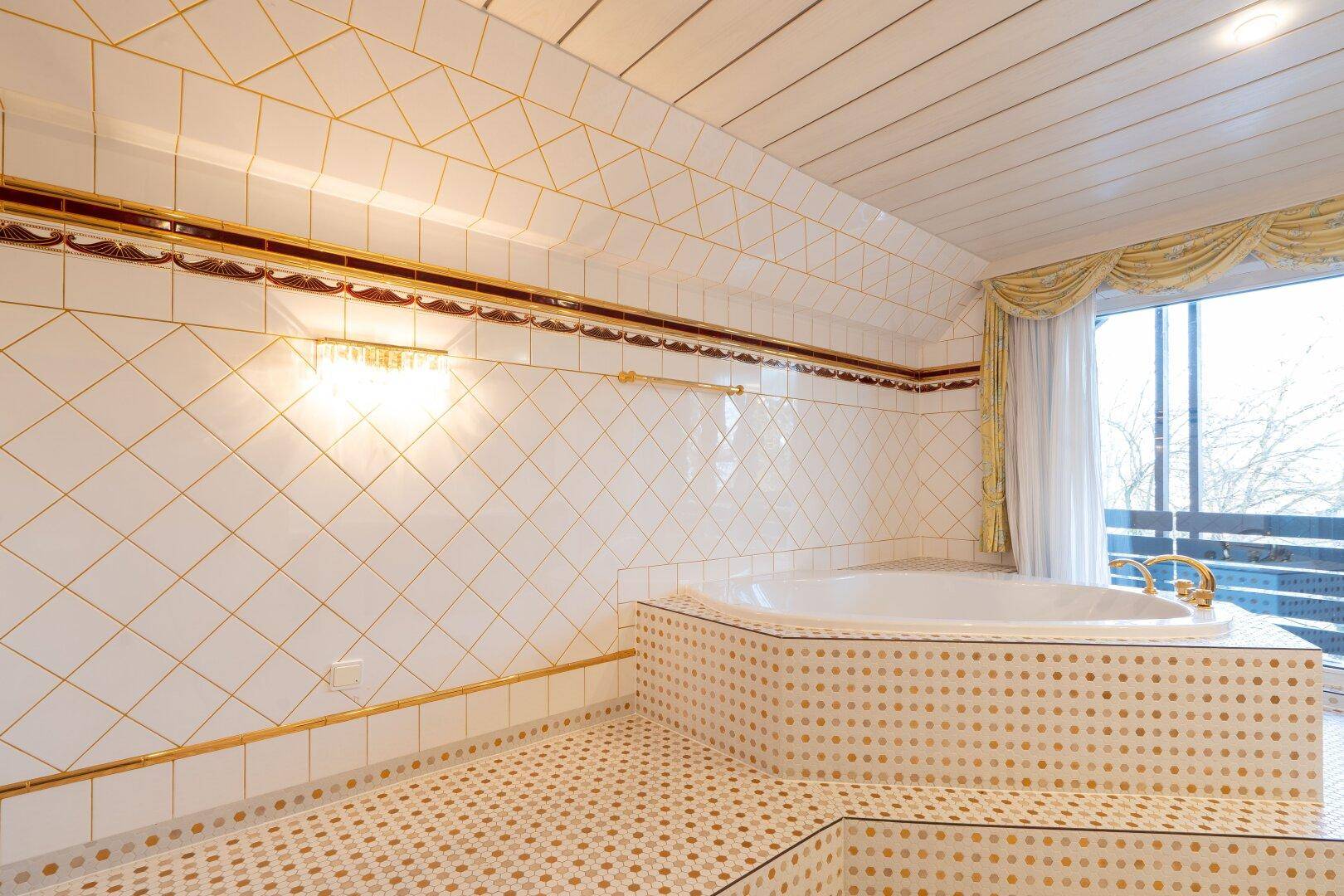 Luxuriöses Badezimmer mit Eckbadewanne, goldenen Armaturen und gemusterten Fliesen, die Eleganz ausstrahlen.