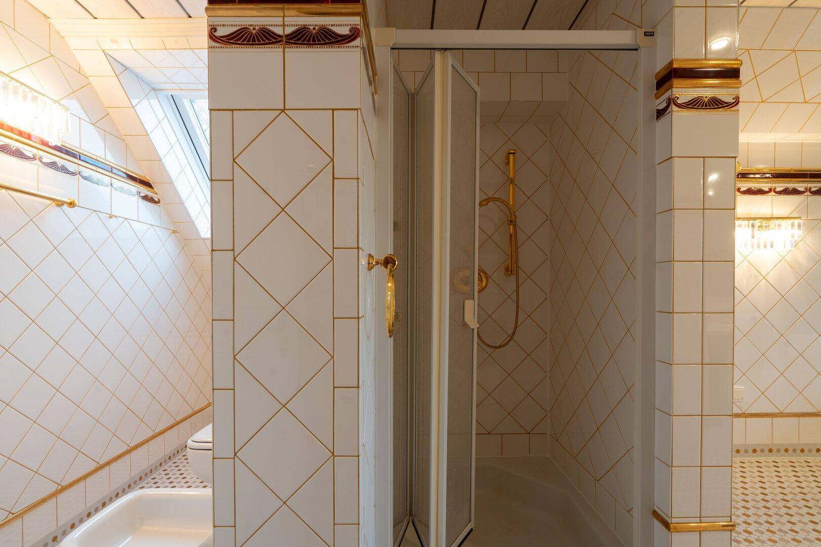 Badezimmer mit Duschkabine, goldenen Armaturen und gemusterten Fliesen, die einen klassischen Stil zeigen.