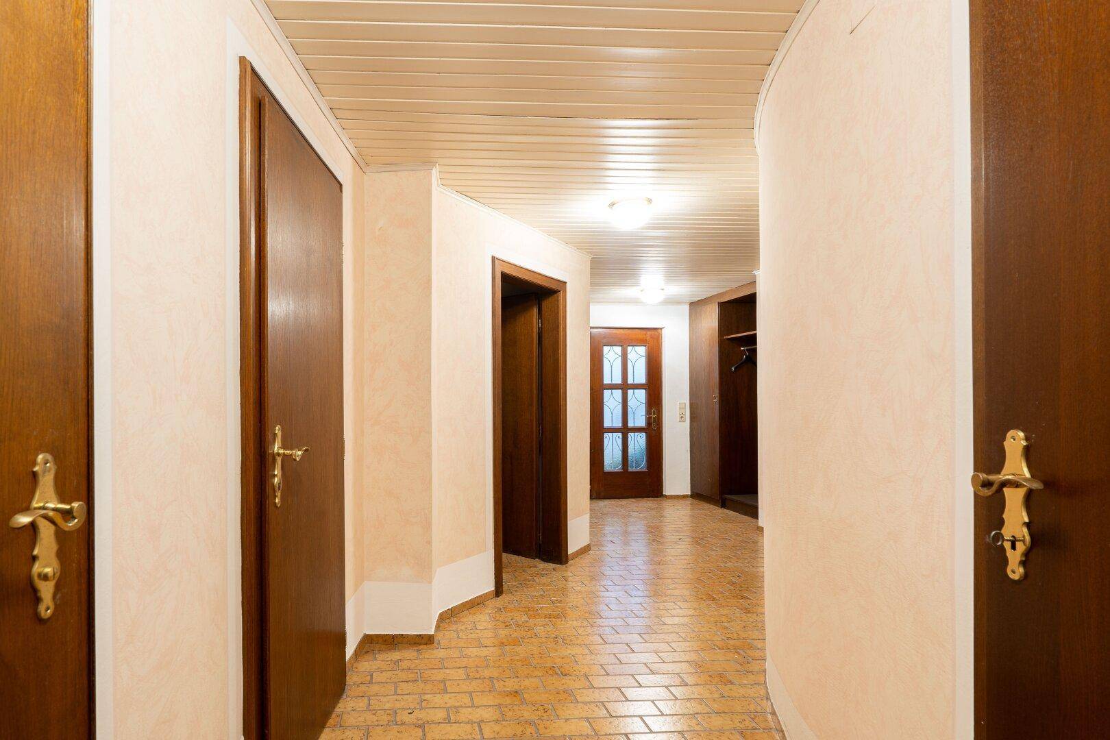 Langer Flur mit Fliesenboden, Holztüren und hellem Ambiente, der die verschiedenen Räume verbindet.