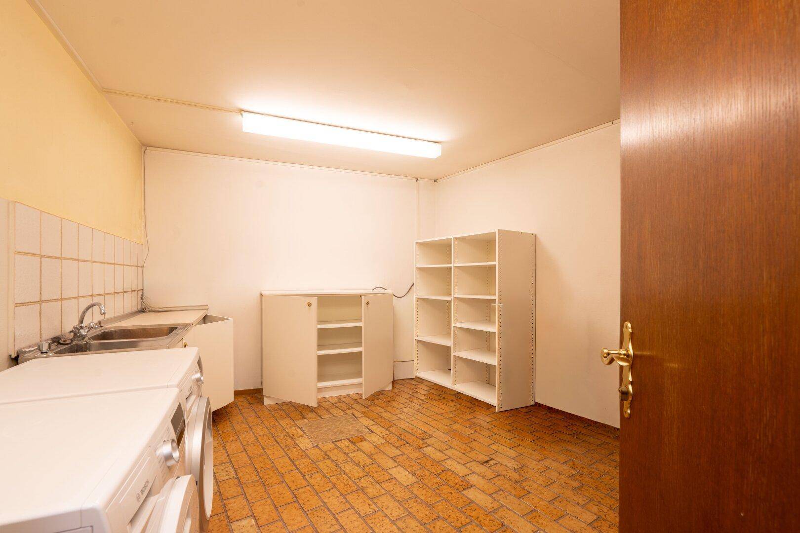 Waschraum im Keller mit Waschmaschinen, Spülbecken und Regalen, der praktische Funktionen bietet.