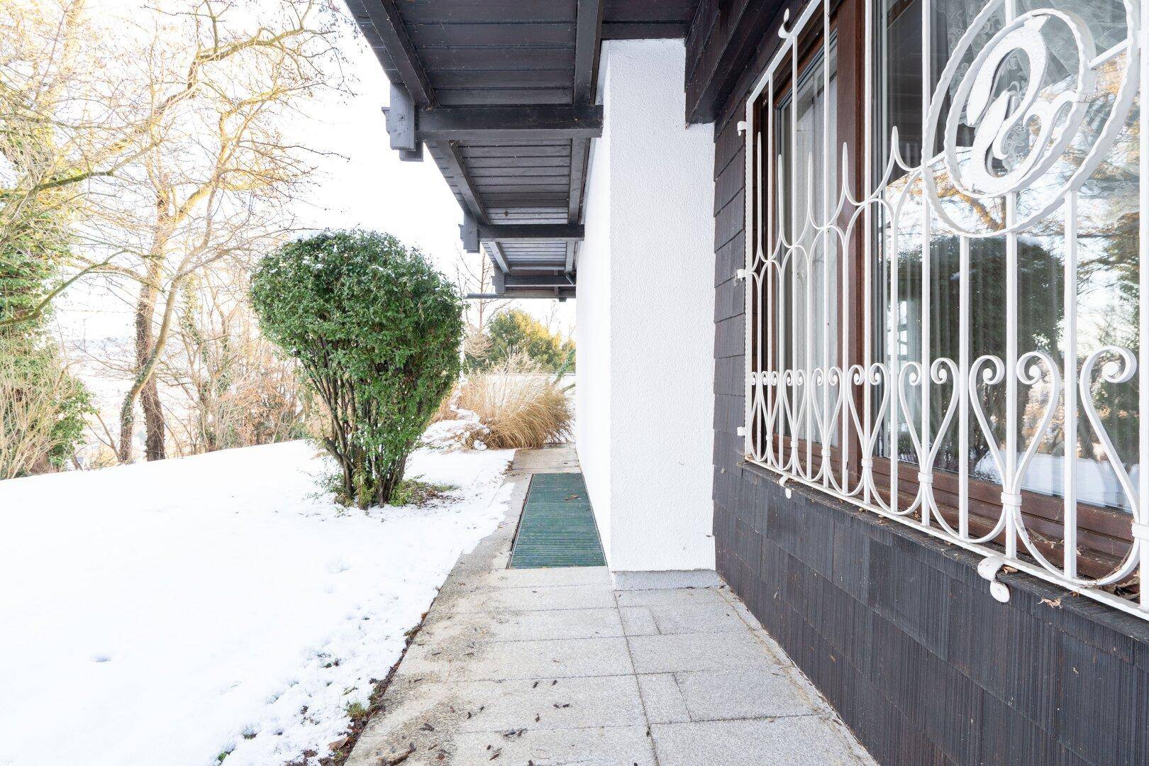 Seitenansicht des Hauses im Winter mit Schnee auf dem Boden und dekorativen Fenstergittern.