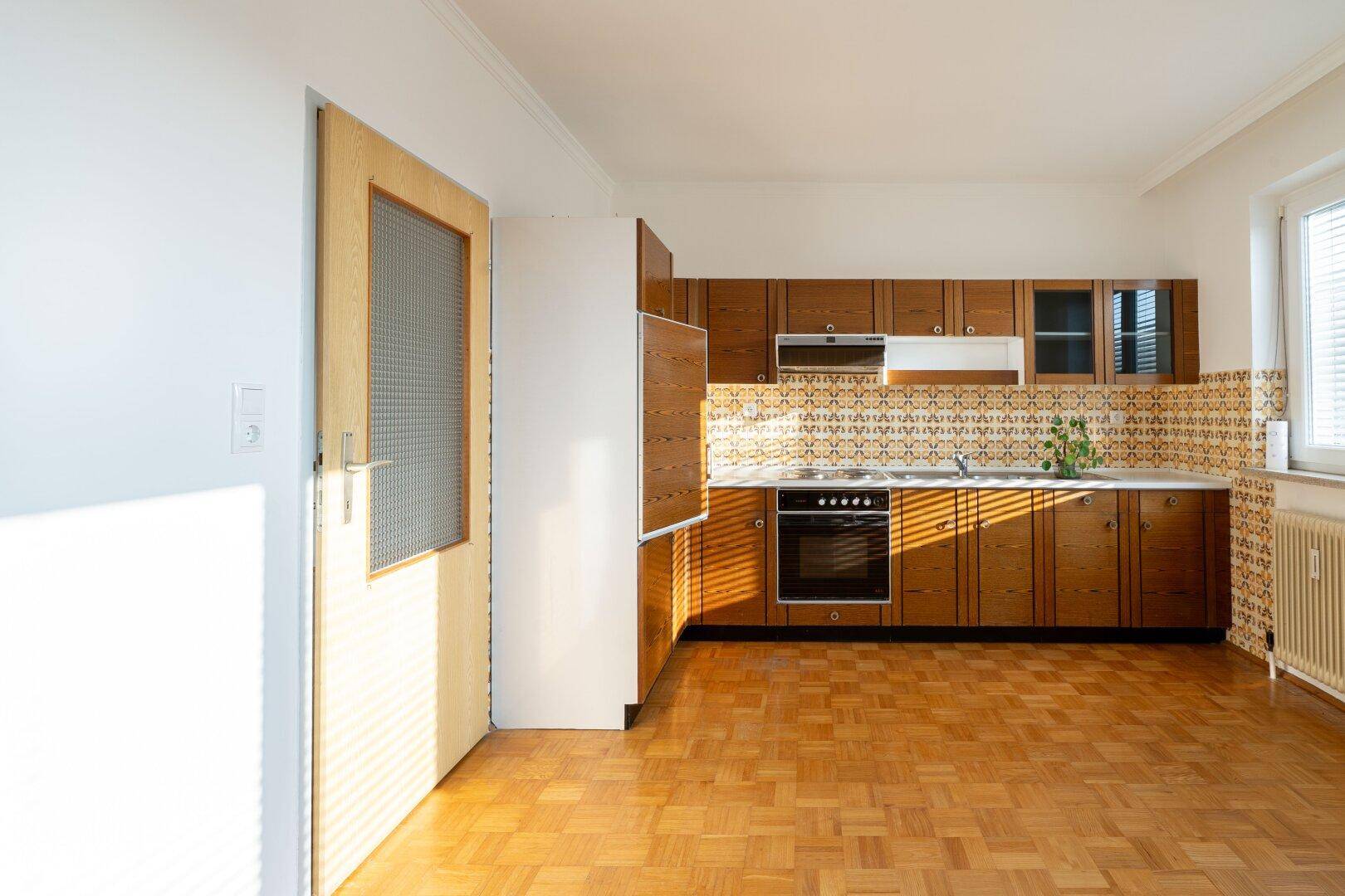 Küche im traditionellen Stil mit Holzschränken, gemusterter Rückwand und Parkettboden, hell beleuchtet.
