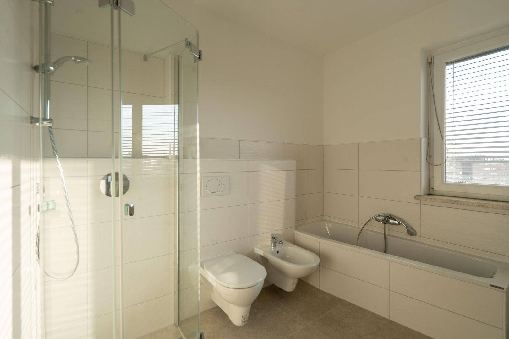 Helles Badezimmer mit Dusche, Badewanne, WC und Bidet, ausgestattet mit Fliesen und einem Fenster.