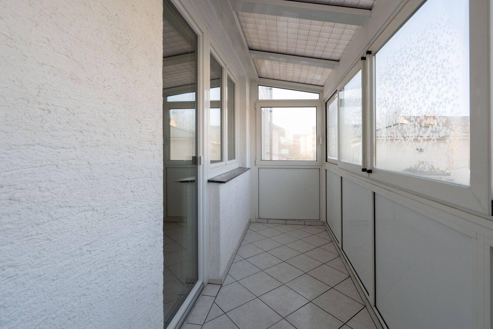 Verglaste Loggia mit Fliesenboden und vielen Fenstern, die einen geschützten Außenbereich bietet.