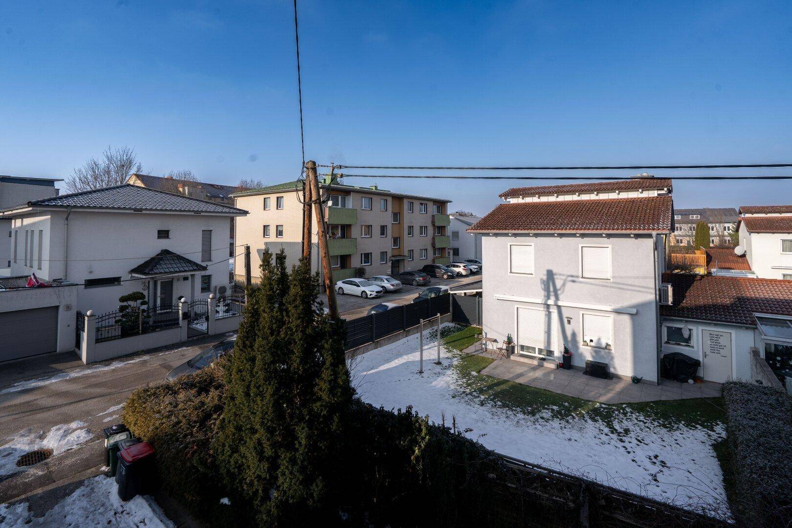 Blick auf eine Wohnsiedlung mit geparkten Autos und einem kleinen Gartenbereich, teilweise mit Schnee bedeckt.