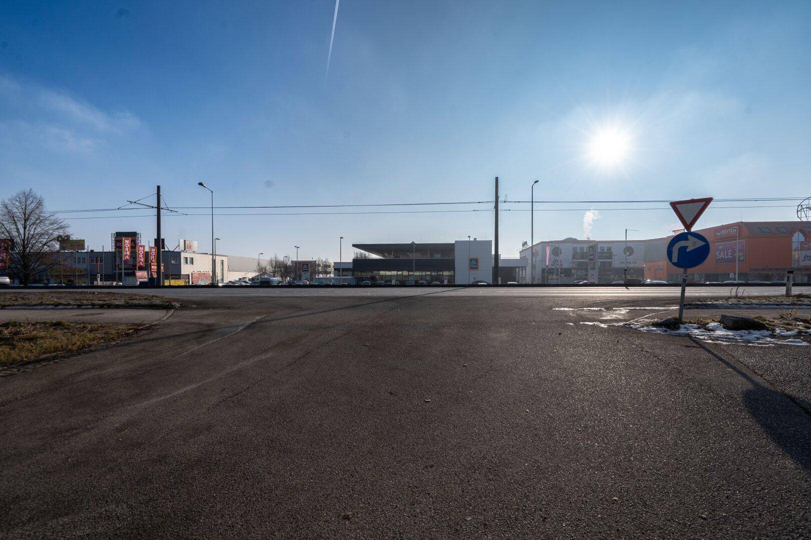 Straßenansicht mit Geschäftsgebäuden im Hintergrund unter einem klaren blauen Himmel.
