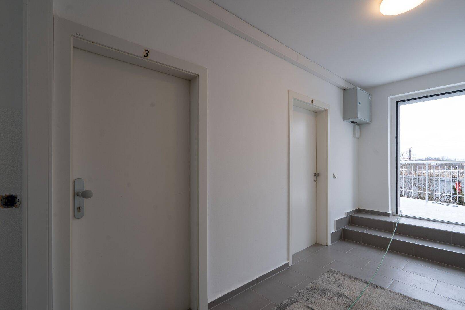 Heller Eingangsbereich mit zwei weißen Türen und einem Treppenaufgang zu den oberen Etagen.