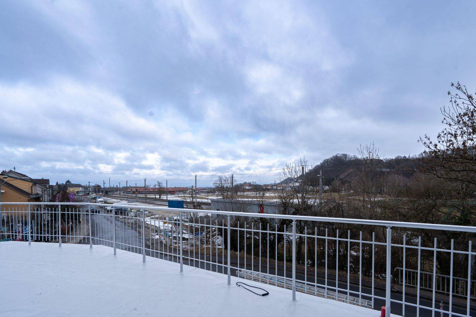 Großer Balkon mit weißem Metallgeländer und weitem Blick auf die Umgebung und Bahngleise.
