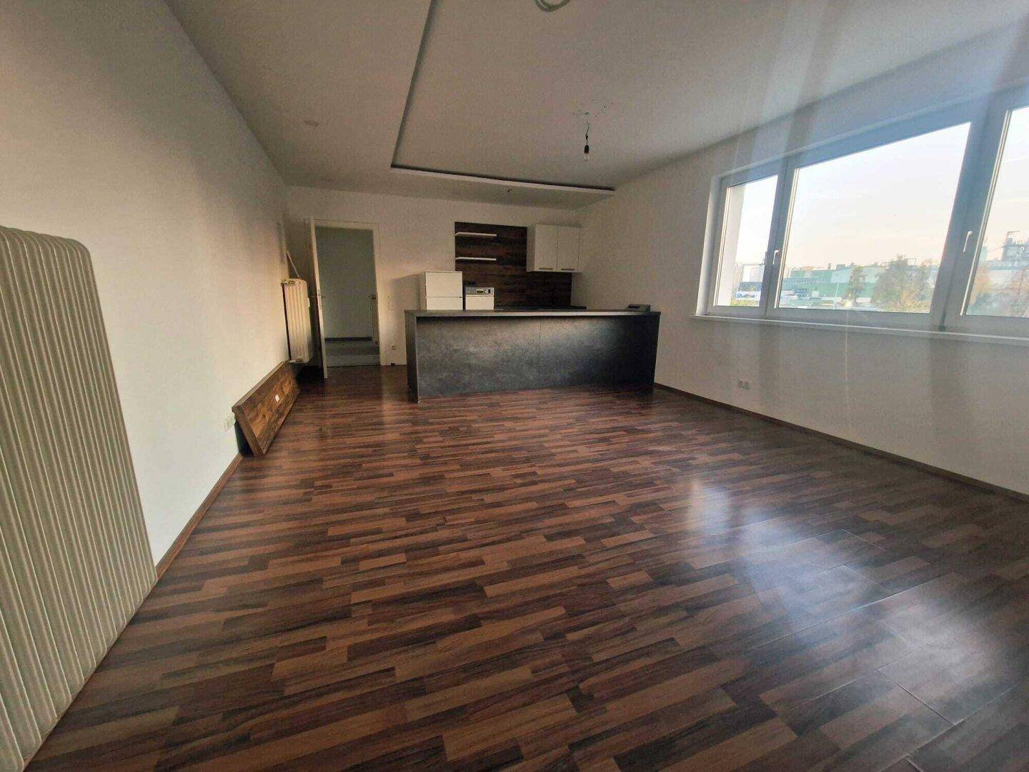 Offener Wohnbereich mit dunklem Laminatboden und einer modernen Küchenbar mit großen Fenstern.