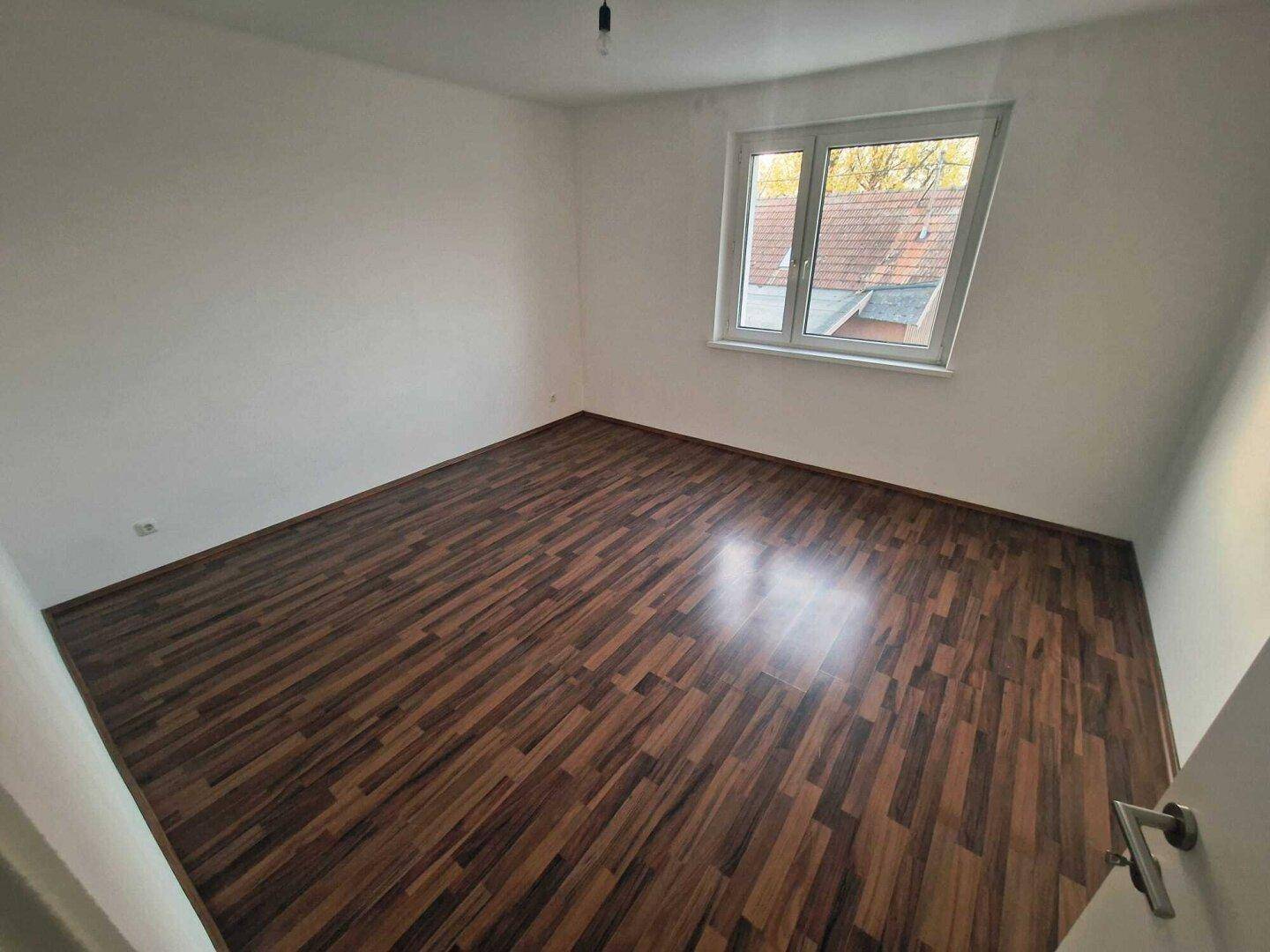Geräumiges Schlafzimmer mit dunklem Laminatboden und einem Fenster, das den Raum erhellt.