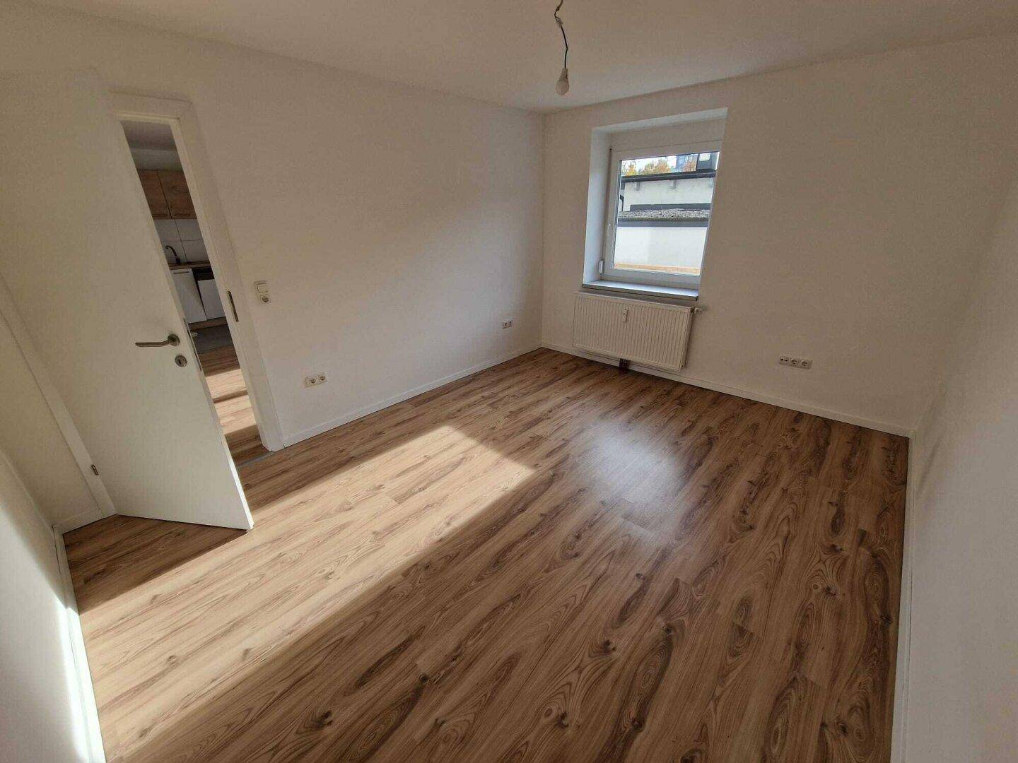 Helles Schlafzimmer mit Laminatboden und einem Fenster, das den Raum mit Tageslicht füllt.