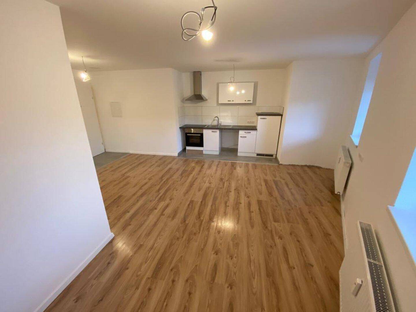 Heller Wohnraum mit Laminatboden und einer funktionalen Küchenzeile an der Wand, ideal für offenes Wohnen.