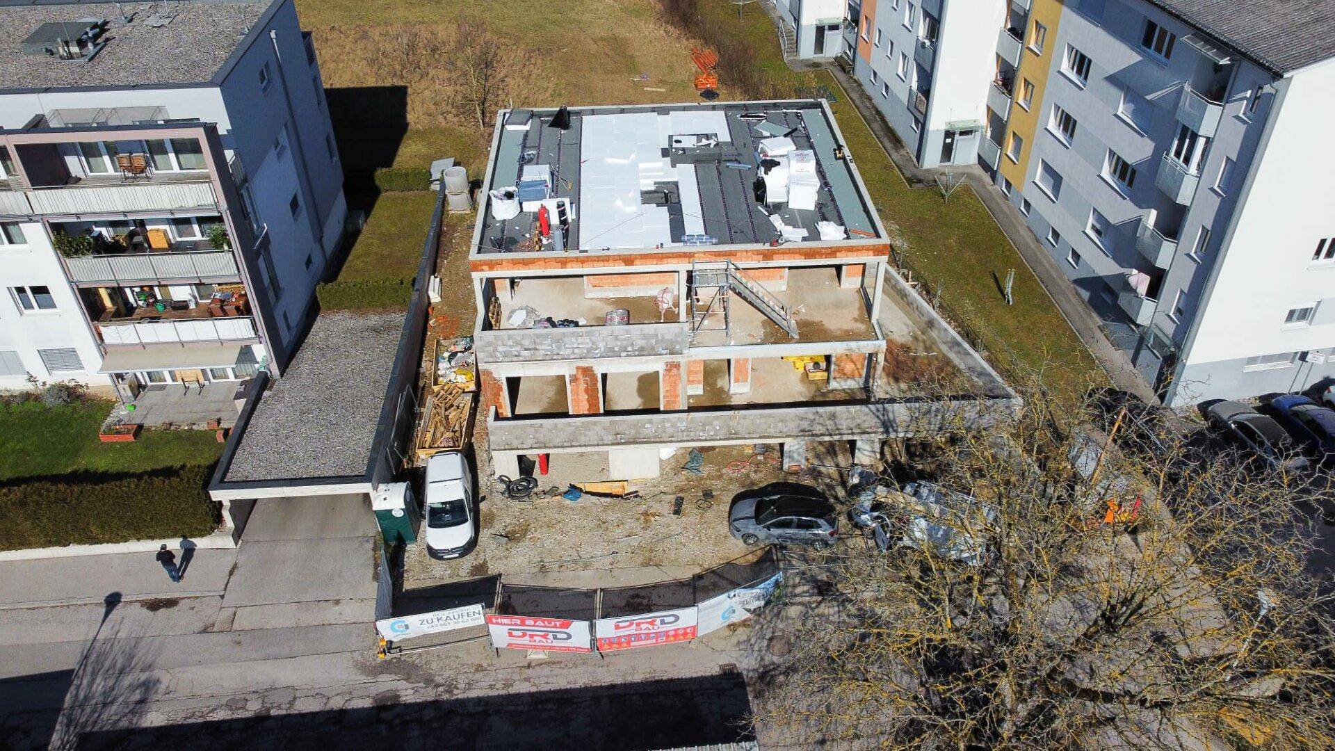 Vogelperspektive einer Baustelle mit Rohbau und umliegenden Wohngebäuden.