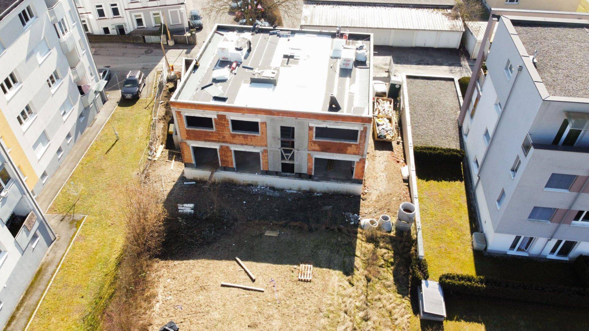 Luftaufnahme einer Baustelle mit Rohbau und angrenzenden Grünflächen.