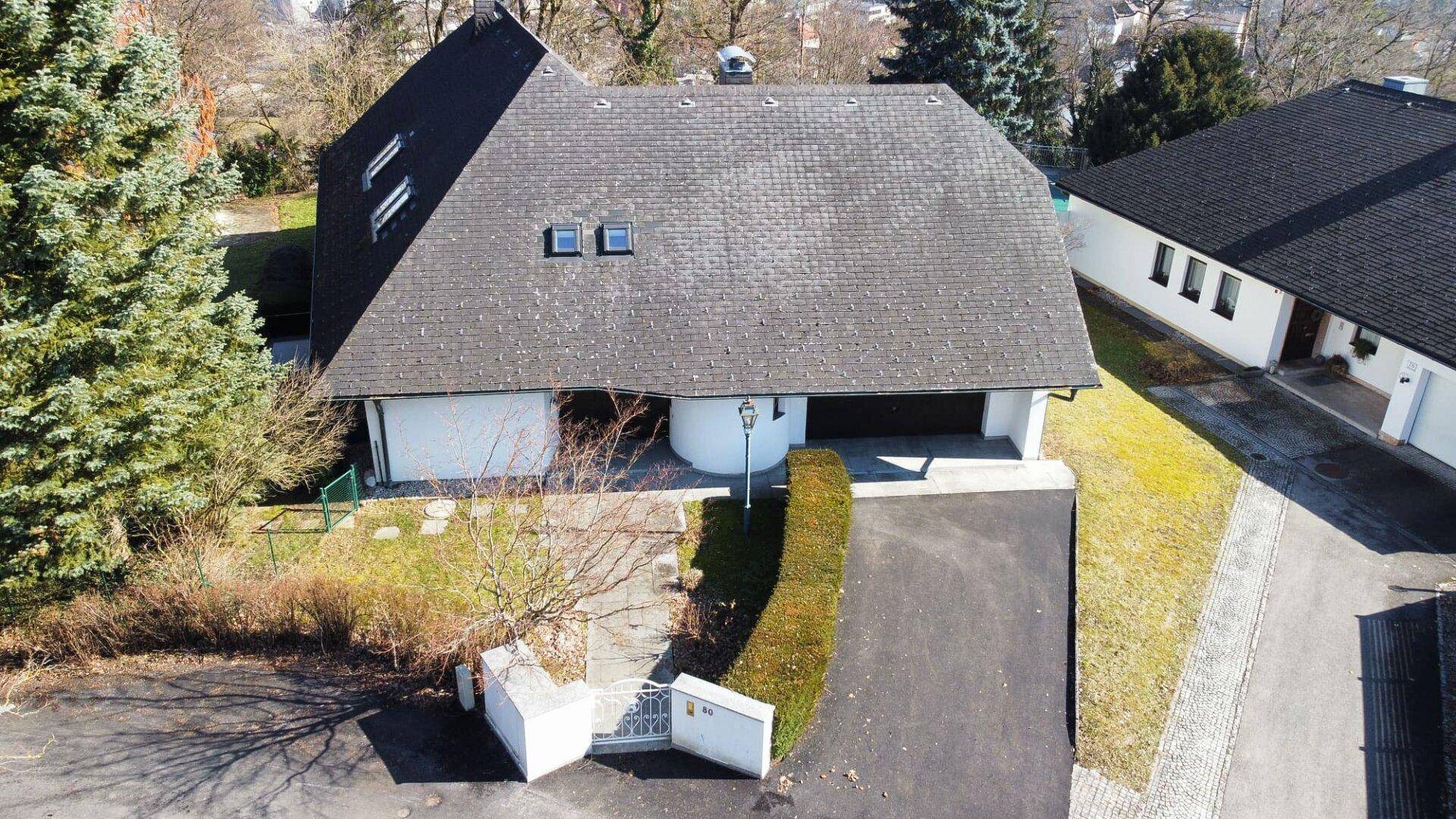 Luftaufnahme eines Einfamilienhauses mit dunklem Dach, weißer Fassade und Zufahrt.