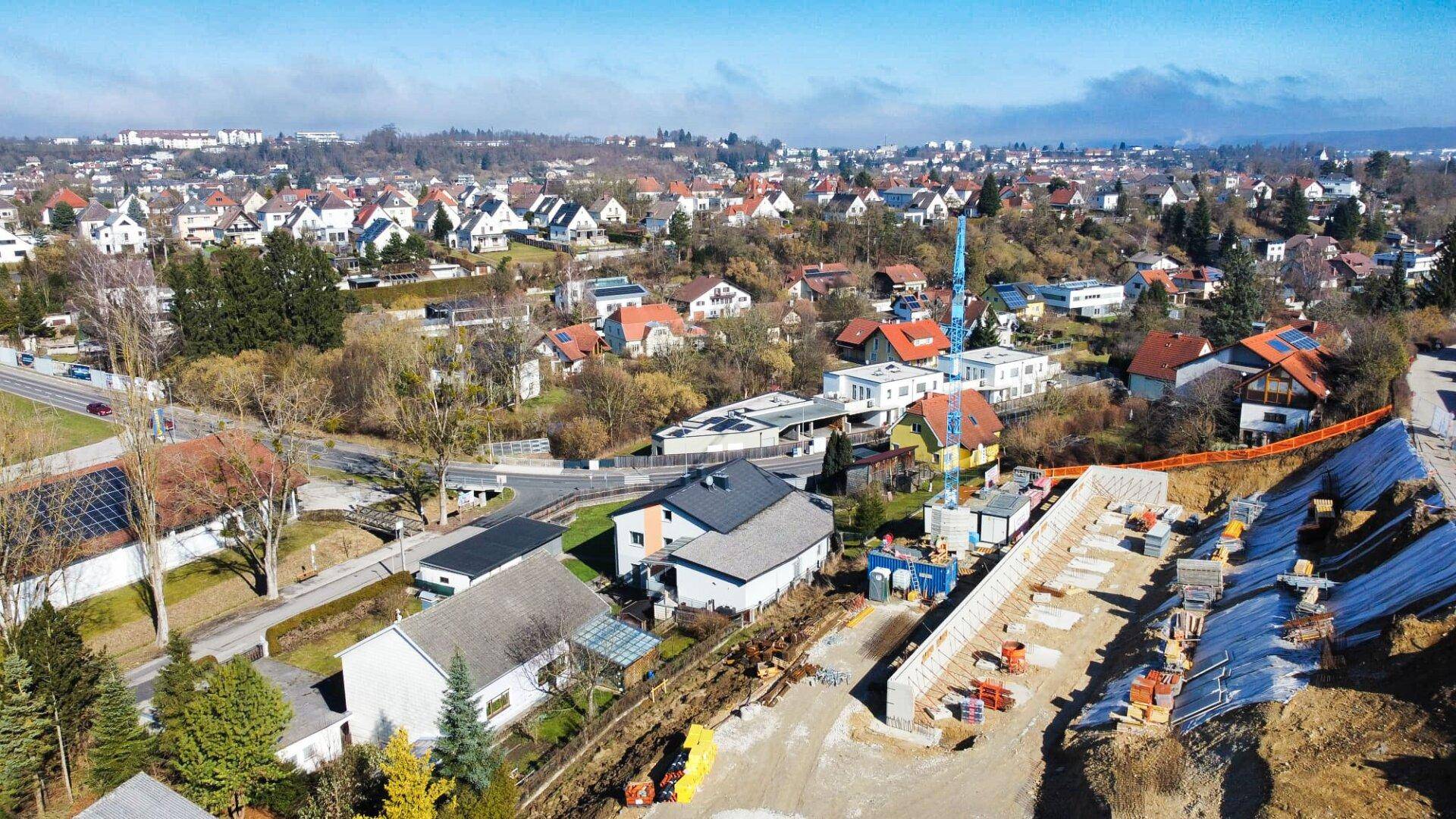 Weitläufige Luftaufnahme einer Baustelle in einer ländlichen Wohngegend mit vielen Dächern und Bäumen.