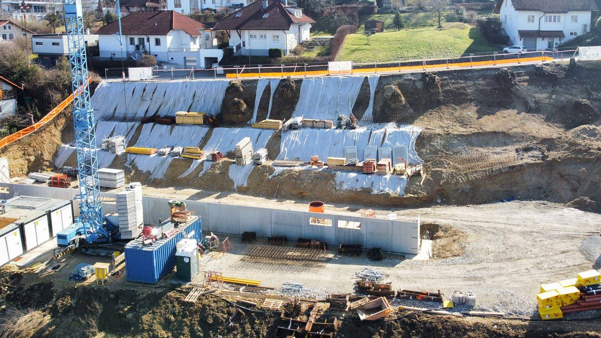 Nahaufnahme einer Baustelle mit Fundamentarbeiten, einem Baukran und einer gesicherten Böschung.
