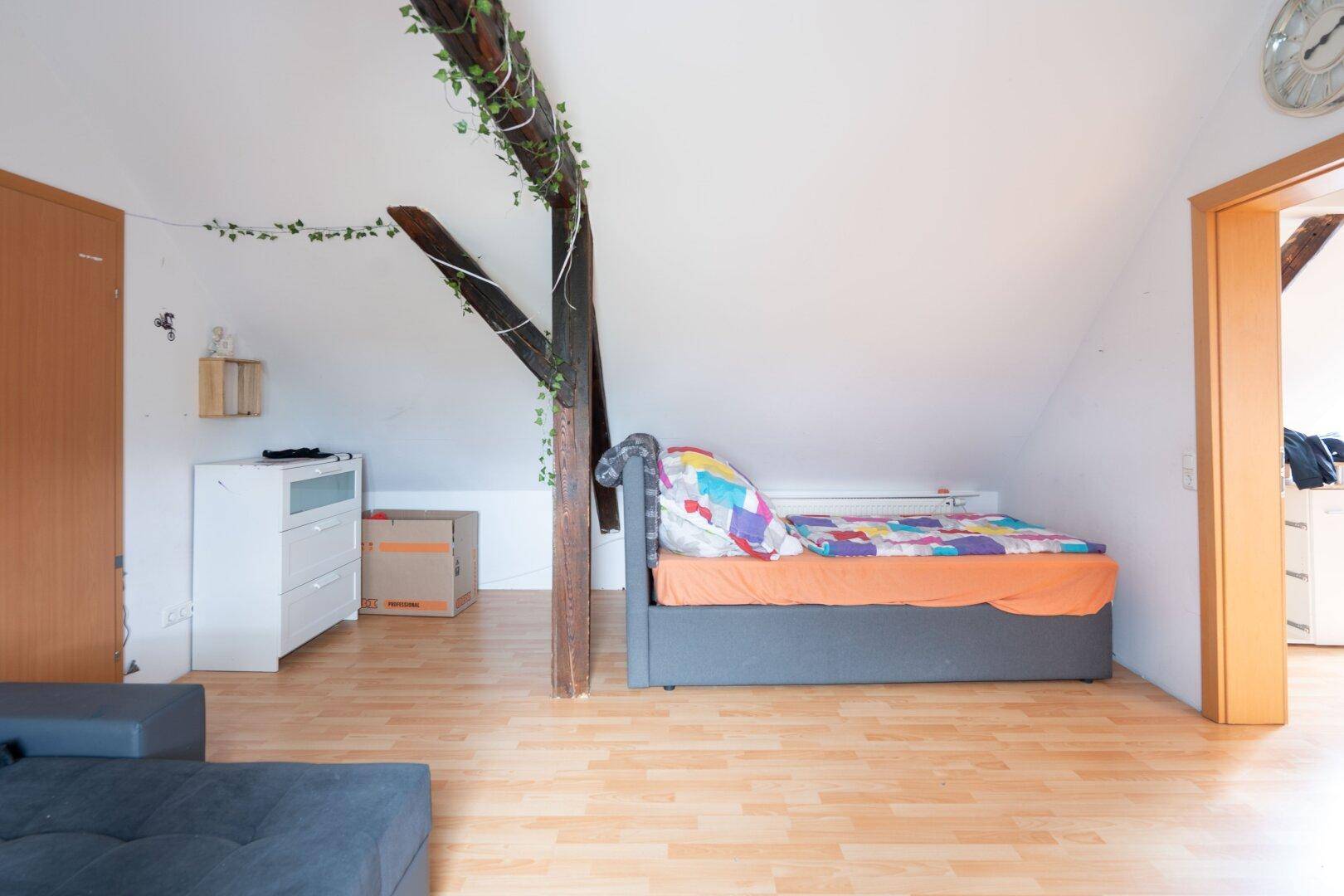 Gemütliches Schlafzimmer im Dachgeschoss mit Holzbalken, schrägen Wänden und Holzboden für eine warme Atmosphäre.
