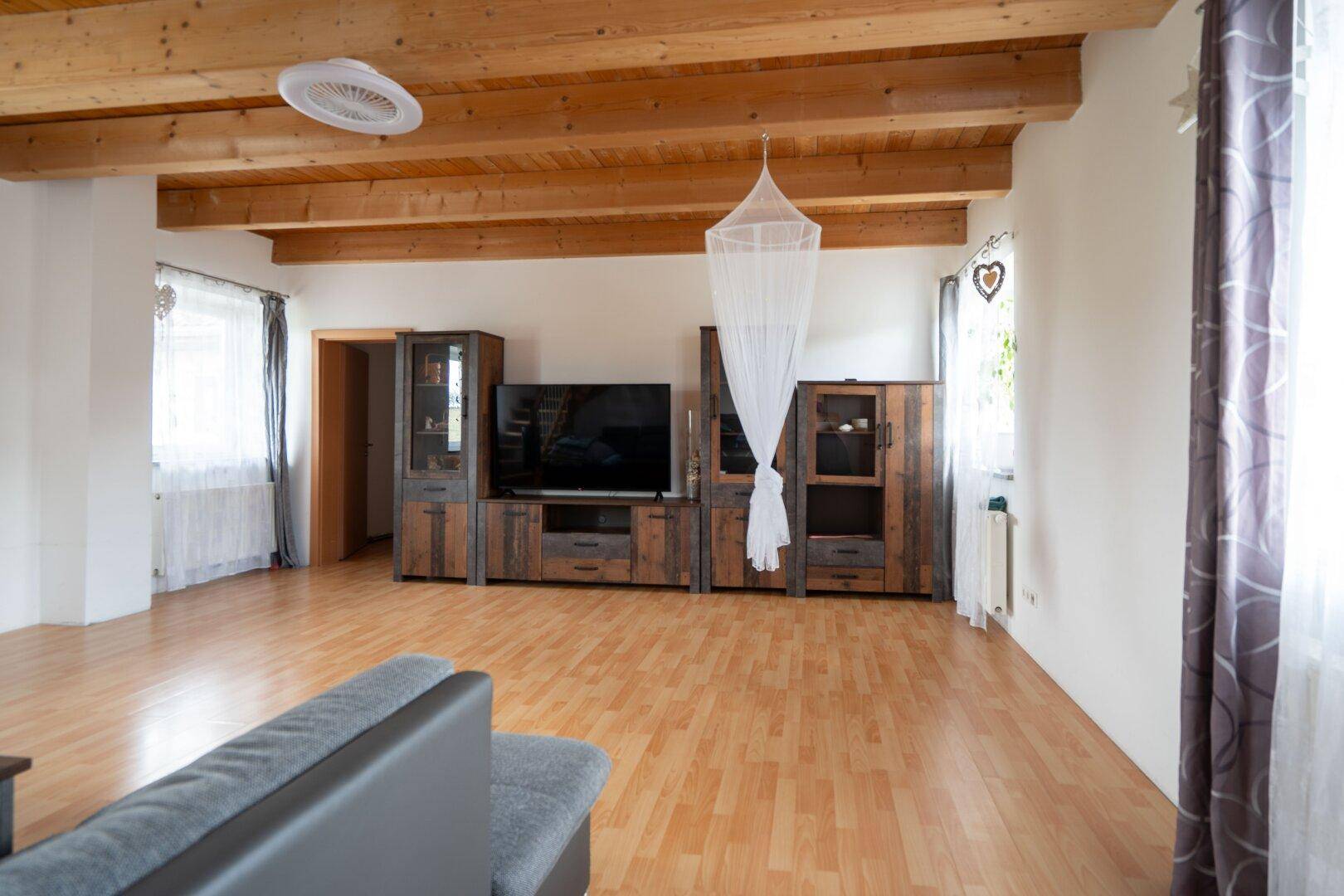 Geräumiges Wohnzimmer mit Holzbalkendecke, Parkettboden und moderner Unterhaltungselektronik für gemütliche Abende.
