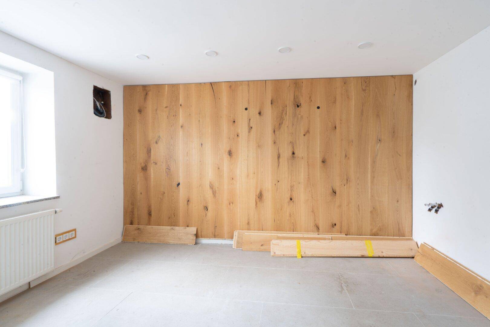 Heller Raum mit Holzwandverkleidung, weißen Wänden und grauen Fliesenboden, der eine warme Atmosphäre schafft.