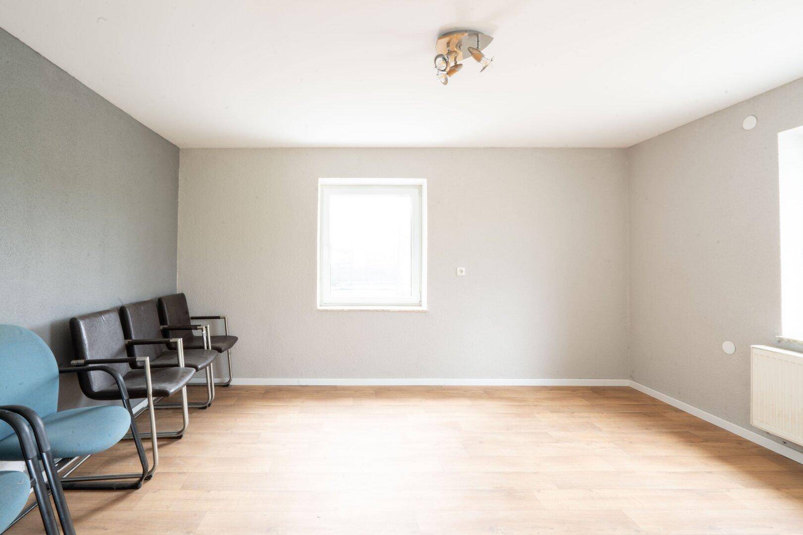 Heller Raum mit Holzboden, grauer Akzentwand und Stühlen, möglicherweise ein Wartebereich oder Büro.