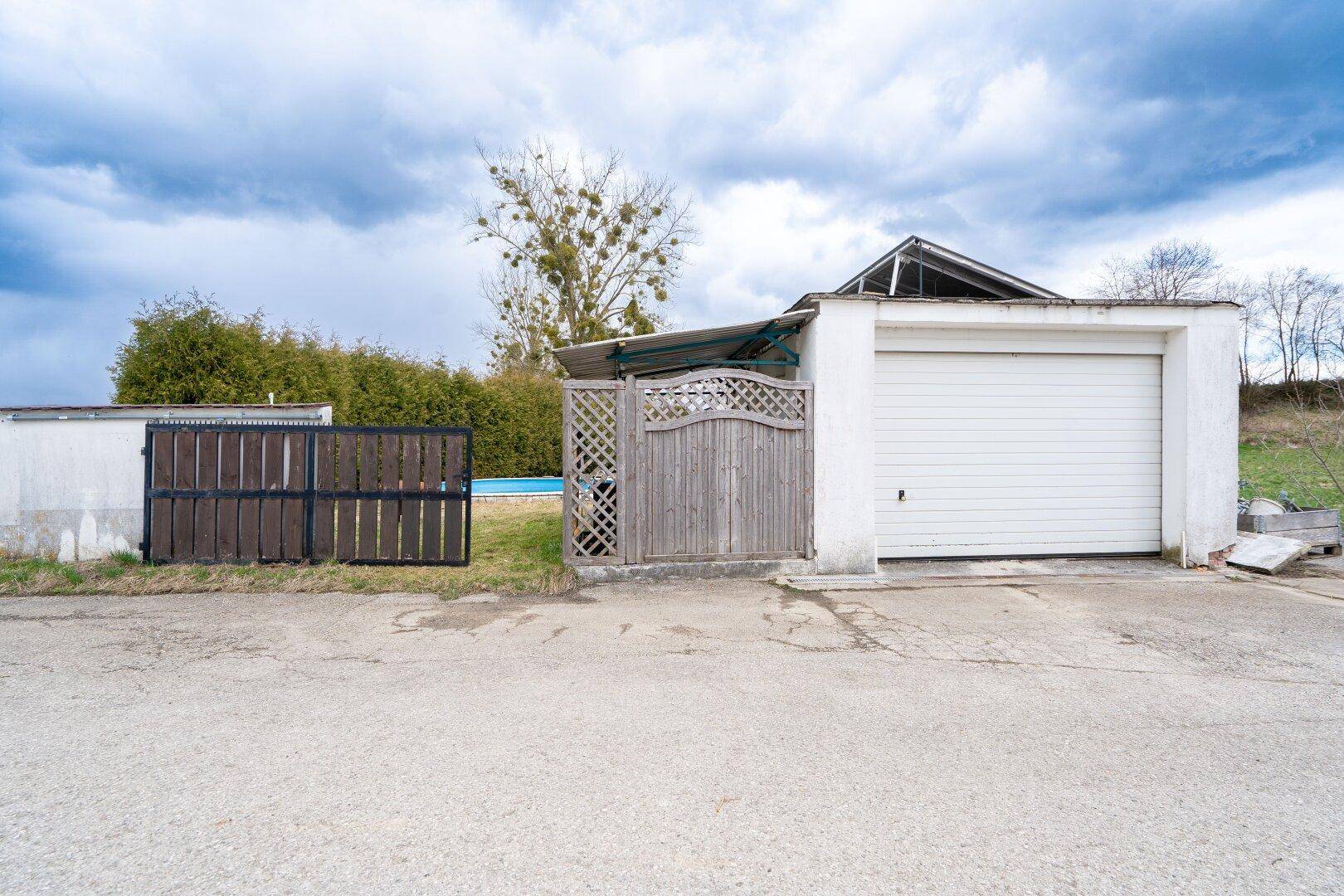 Außenansicht mit Garage, Holzzaun und Zugang zum hinteren Grundstücksbereich.