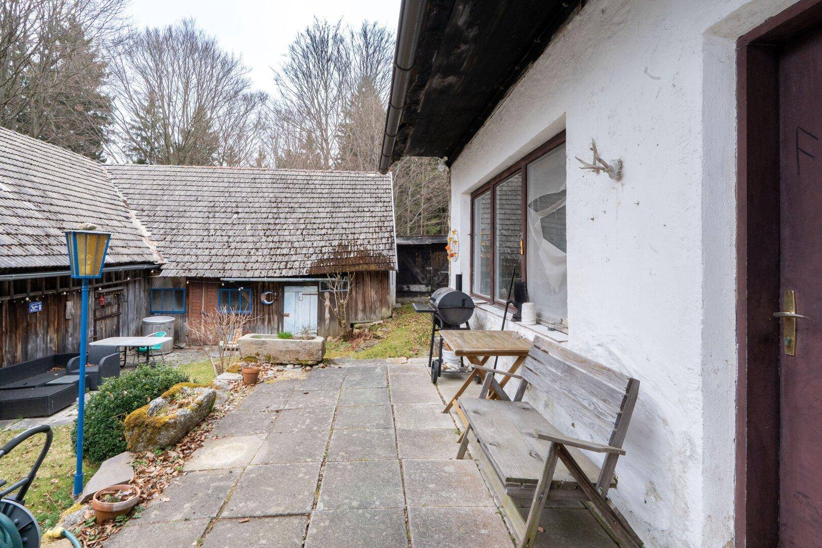 Gepflasterte Terrasse mit Holzbänken und Grillbereich vor dem rustikalen Bauernhaus.