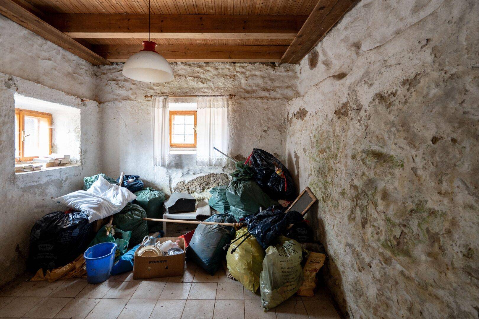 Abstellraum mit vielen Säcken und Gegenständen, rustikale Steinwände und kleine Fenster.