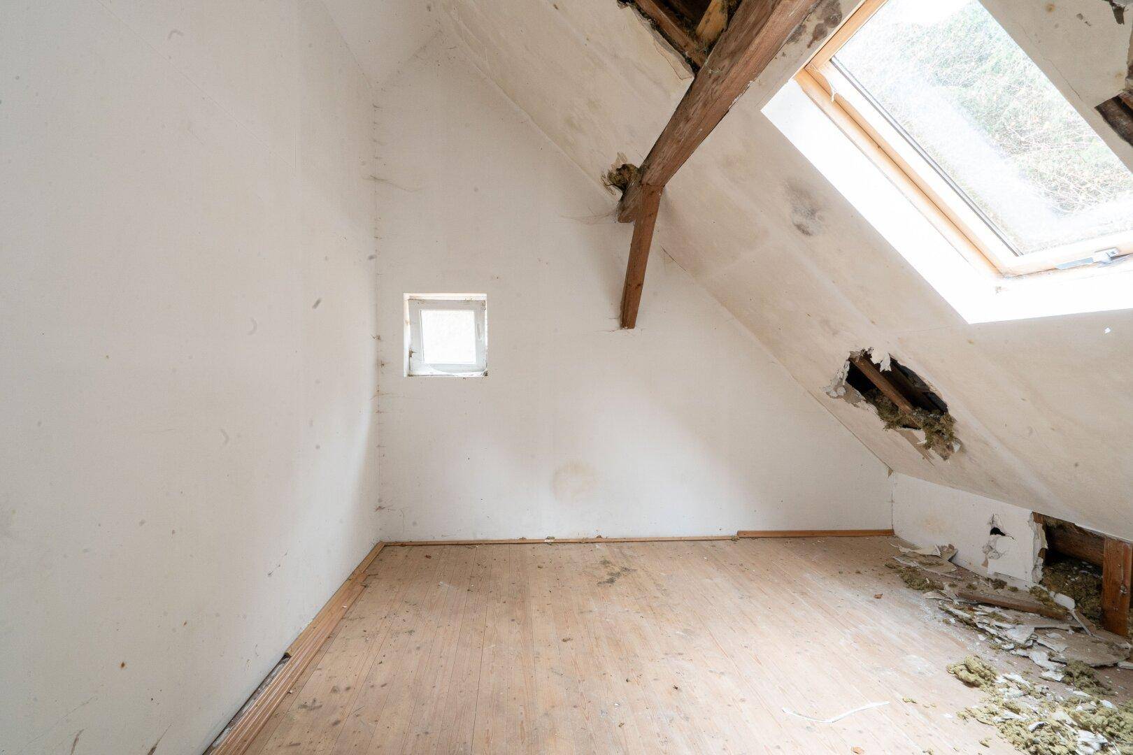 Unausgebauter Dachraum mit schrägen Wänden und Dachfenster, bietet Ausbaupotenzial.