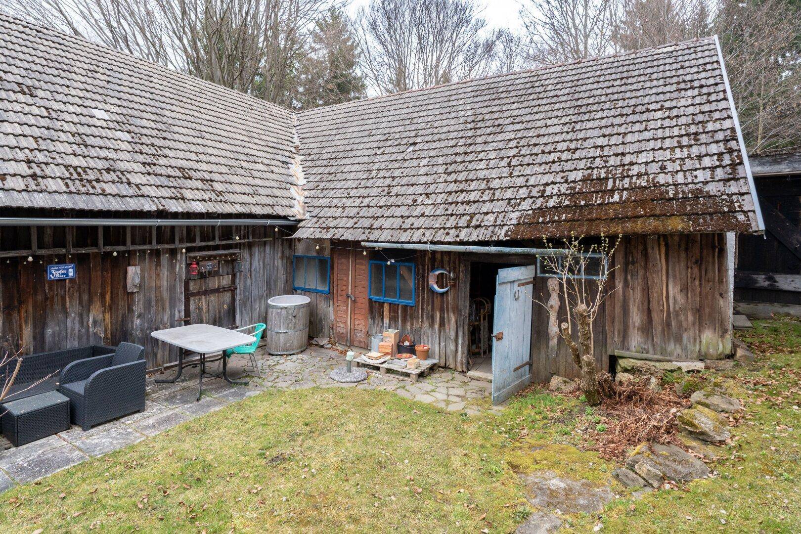 Rustikaler Innenhof mit Holzhütte und Sitzgelegenheiten, umgeben von alten Gebäuden.