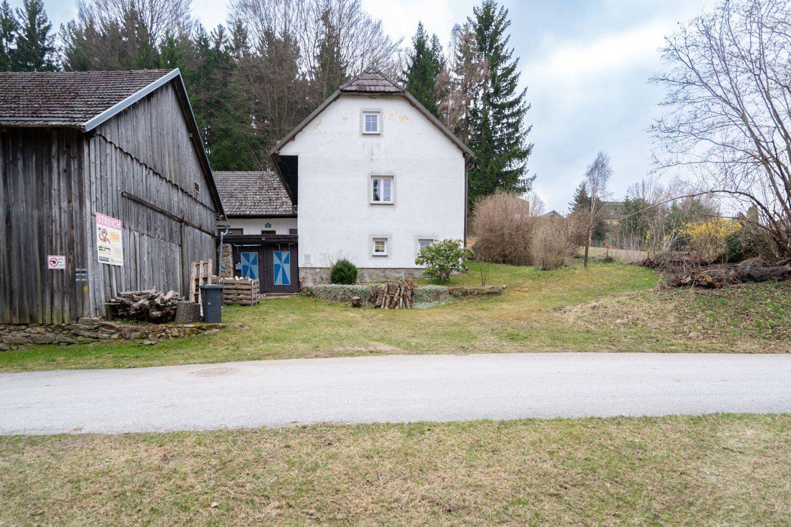 Freistehendes Bauernhaus mit weißer Fassade und umliegender Grünfläche in ländlicher Umgebung.