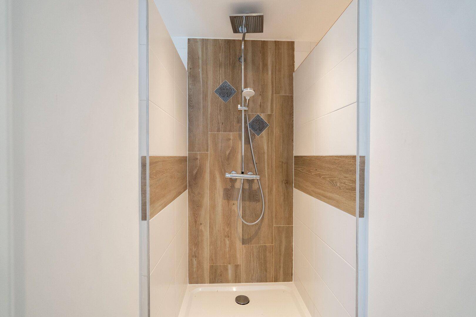 Moderne Duschkabine mit Holzoptik-Fliesen und Regendusche, die ein entspannendes Erlebnis bietet.