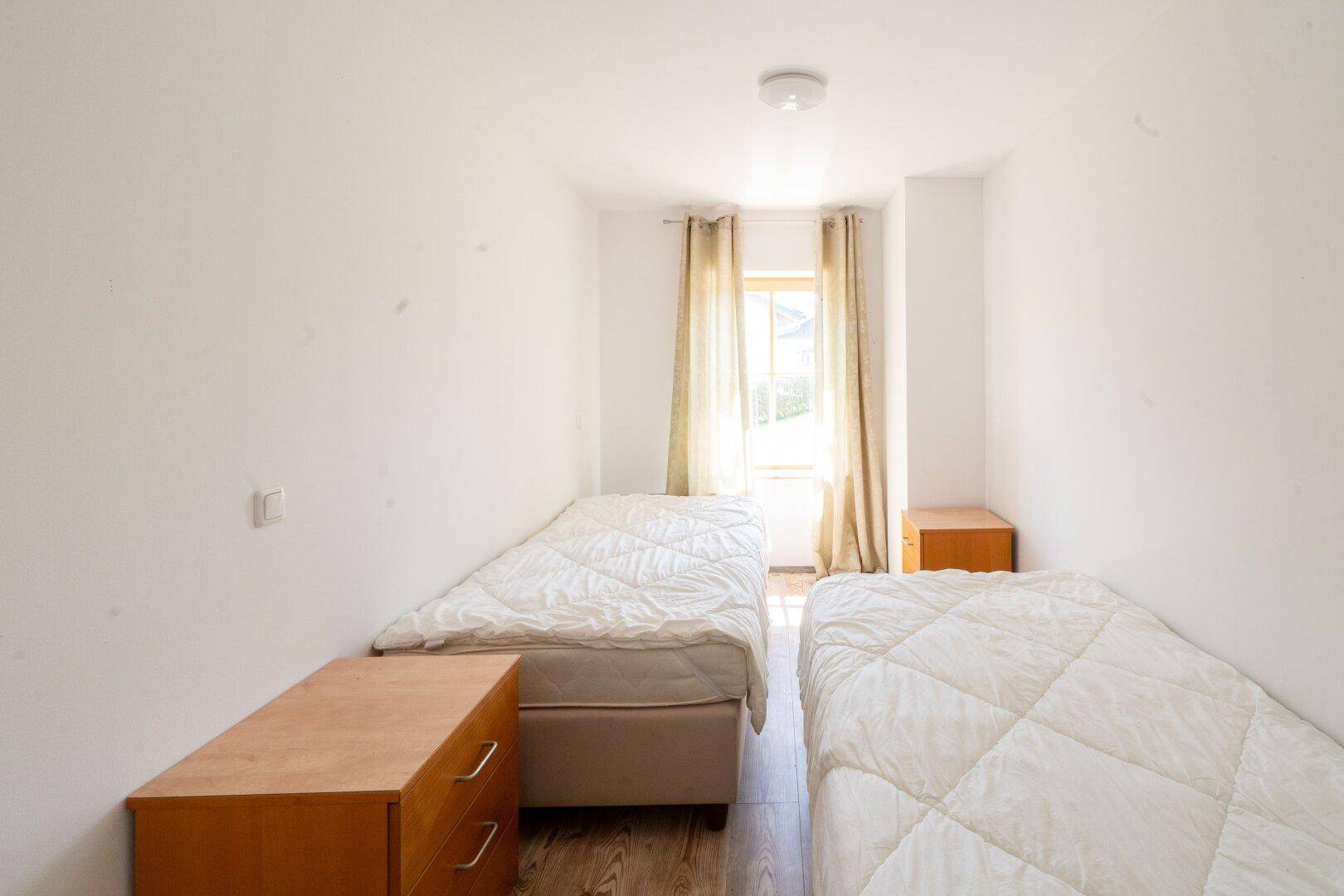 Helles Schlafzimmer mit zwei Einzelbetten und Holzboden, das eine einfache und funktionale Einrichtung bietet.