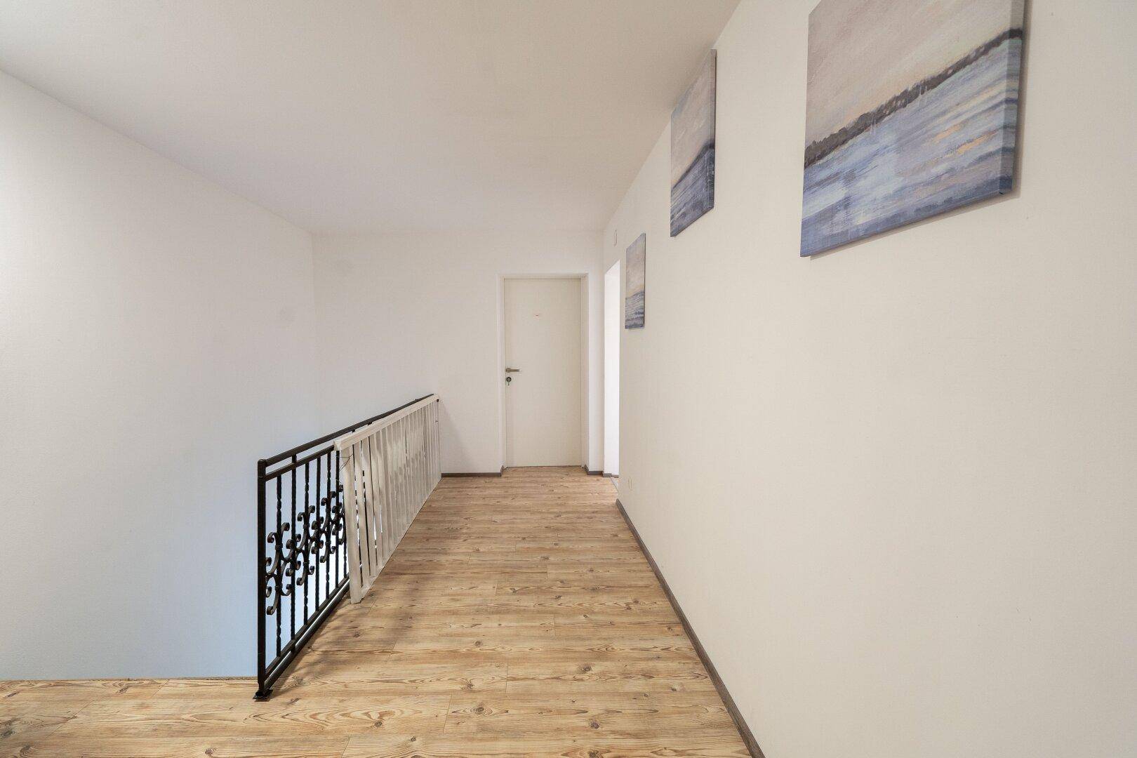 Heller Flur im Obergeschoss mit Holzfußboden und Treppengeländer, der zu weiteren Räumen führt.