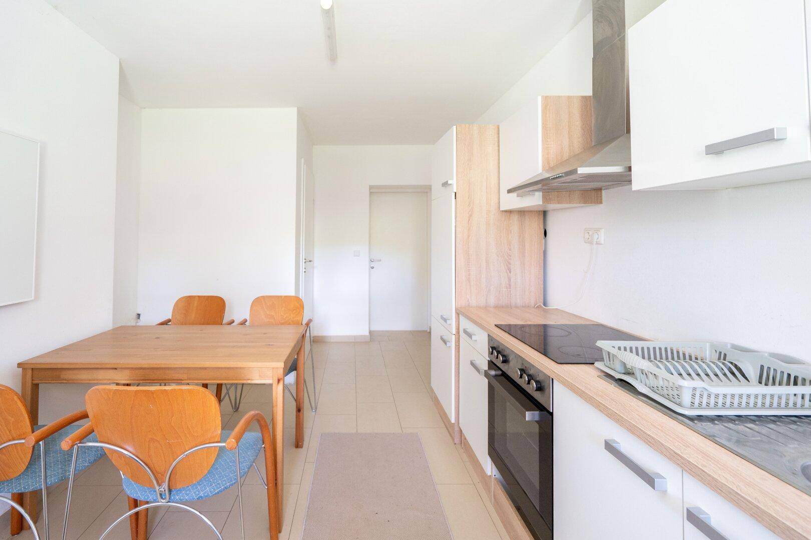 Moderne Einbauküche mit hellem Holzdekor, Essbereich und Fliesenboden, ideal für den Alltag.