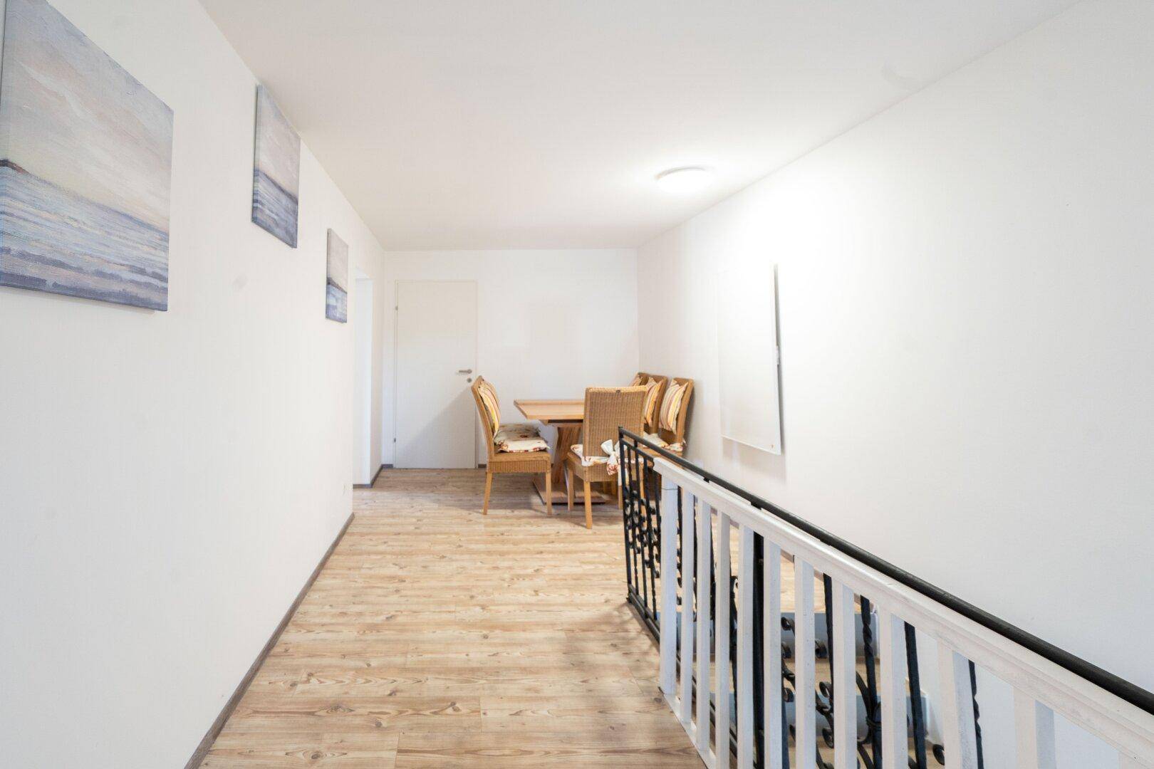 Heller Flur im Obergeschoss mit Holzfußboden und Treppengeländer, der zu weiteren Räumen führt.