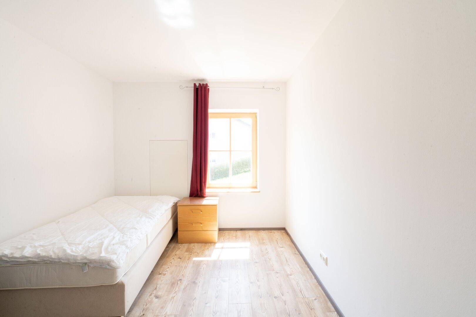 Helles Schlafzimmer mit Einzelbett und Holzboden, das viel Tageslicht durch das Fenster erhält.