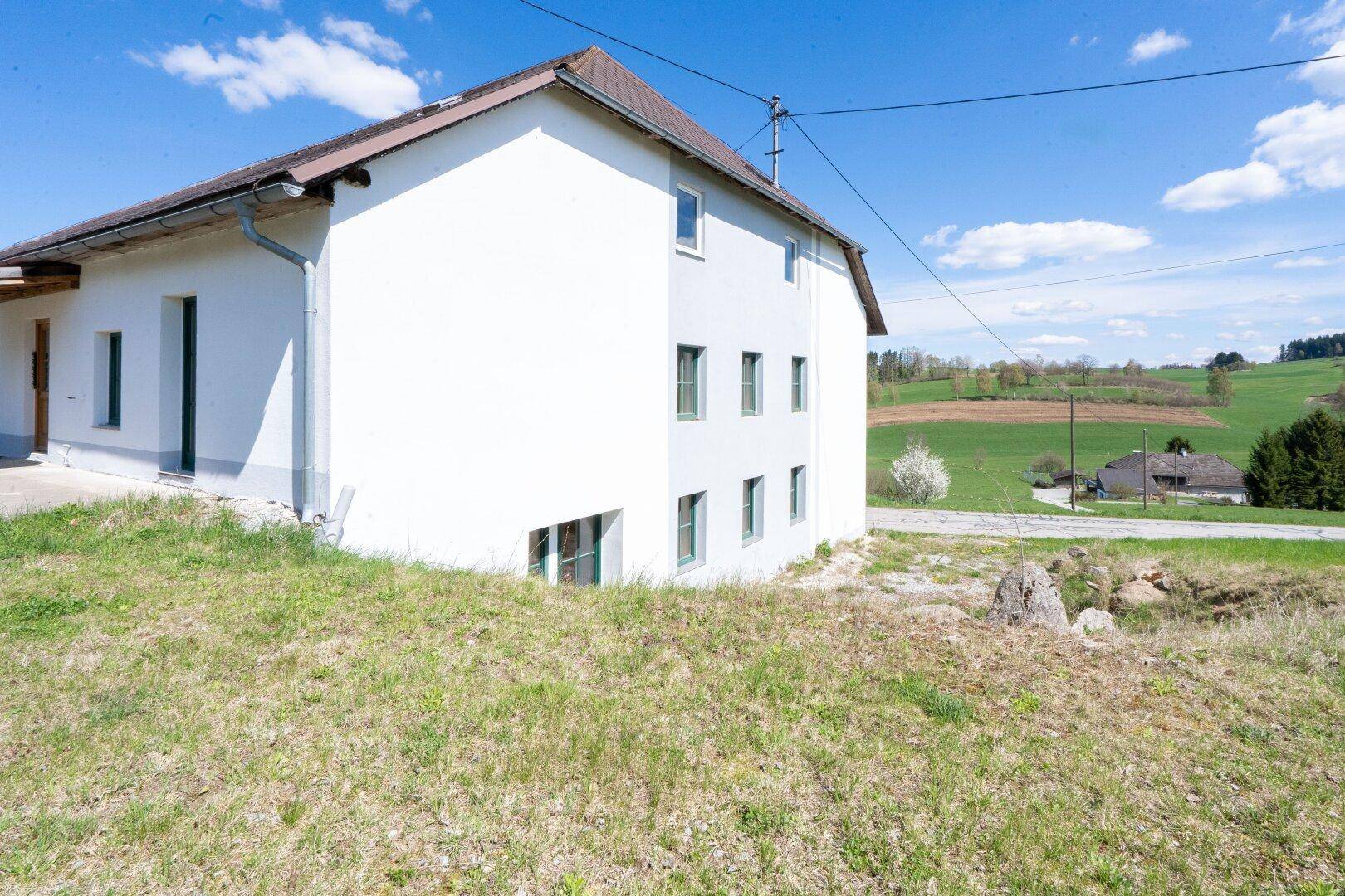 Seitenansicht des Gebäudes mit weißer Fassade, grüner Wiese und weitem Blick über die Landschaft.