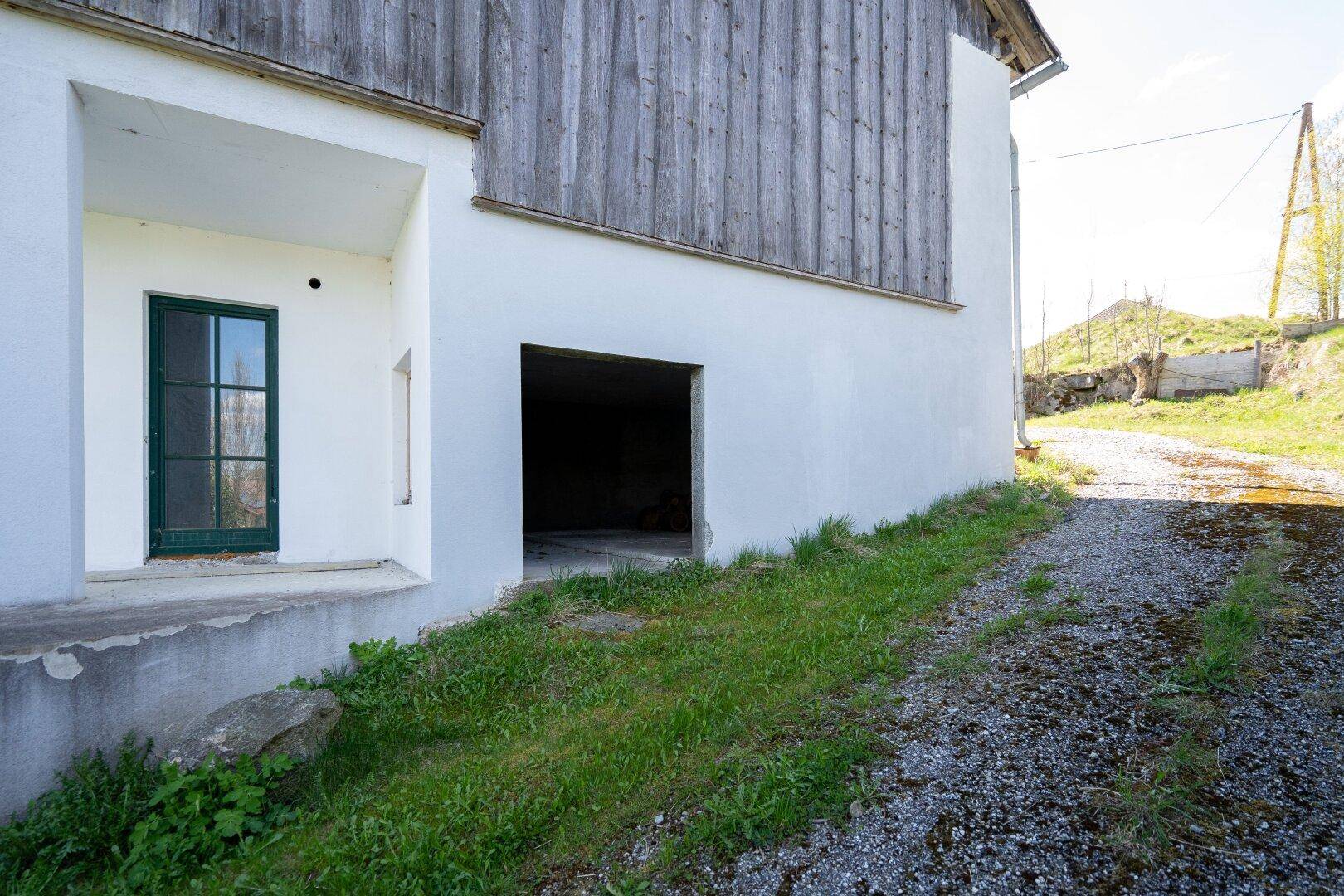 Unterer Bereich eines Gebäudes mit grüner Tür und offenem Garagentor, umgeben von Gras.