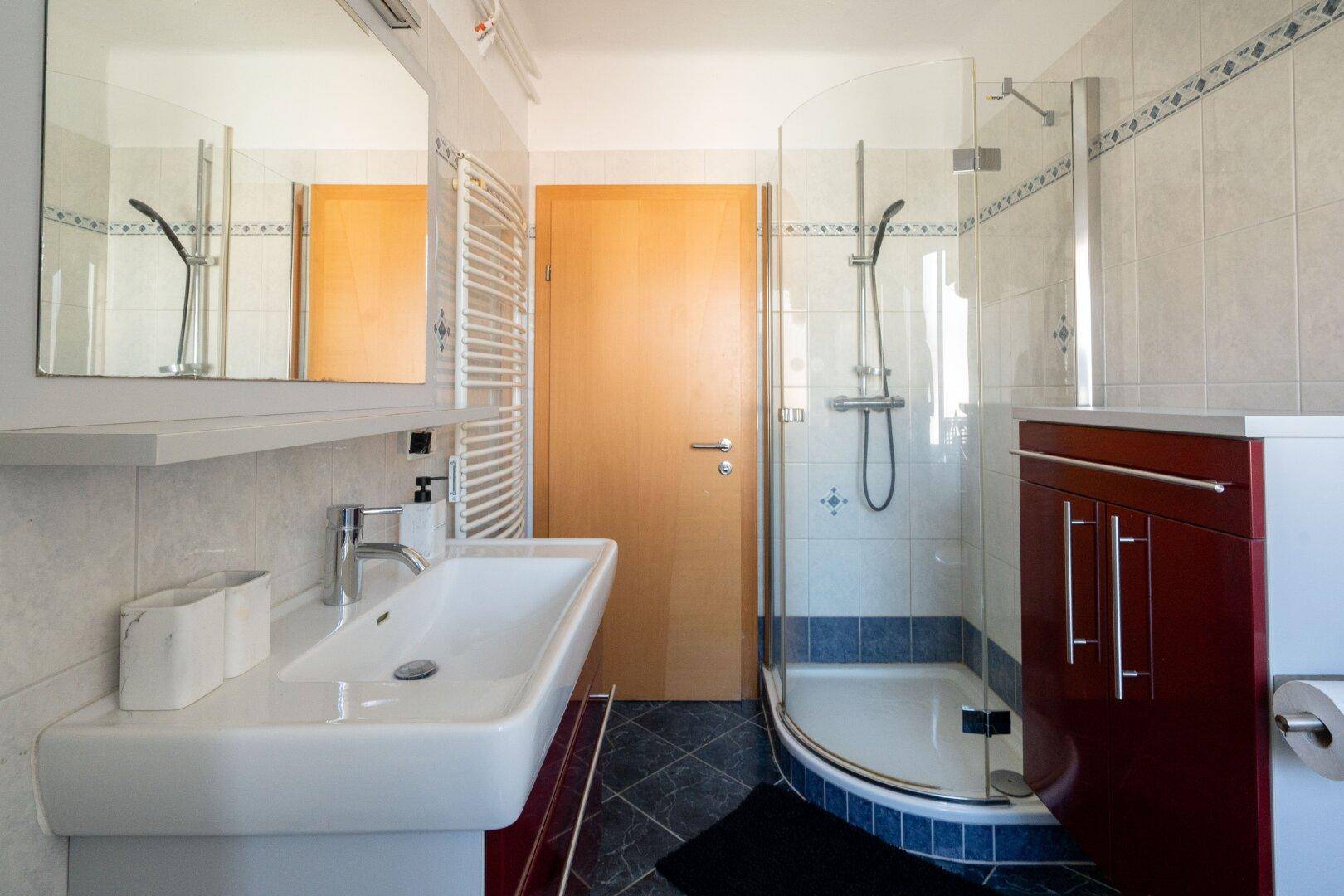 Modernes Badezimmer mit Duschkabine, Waschbecken und beheiztem Handtuchhalter.