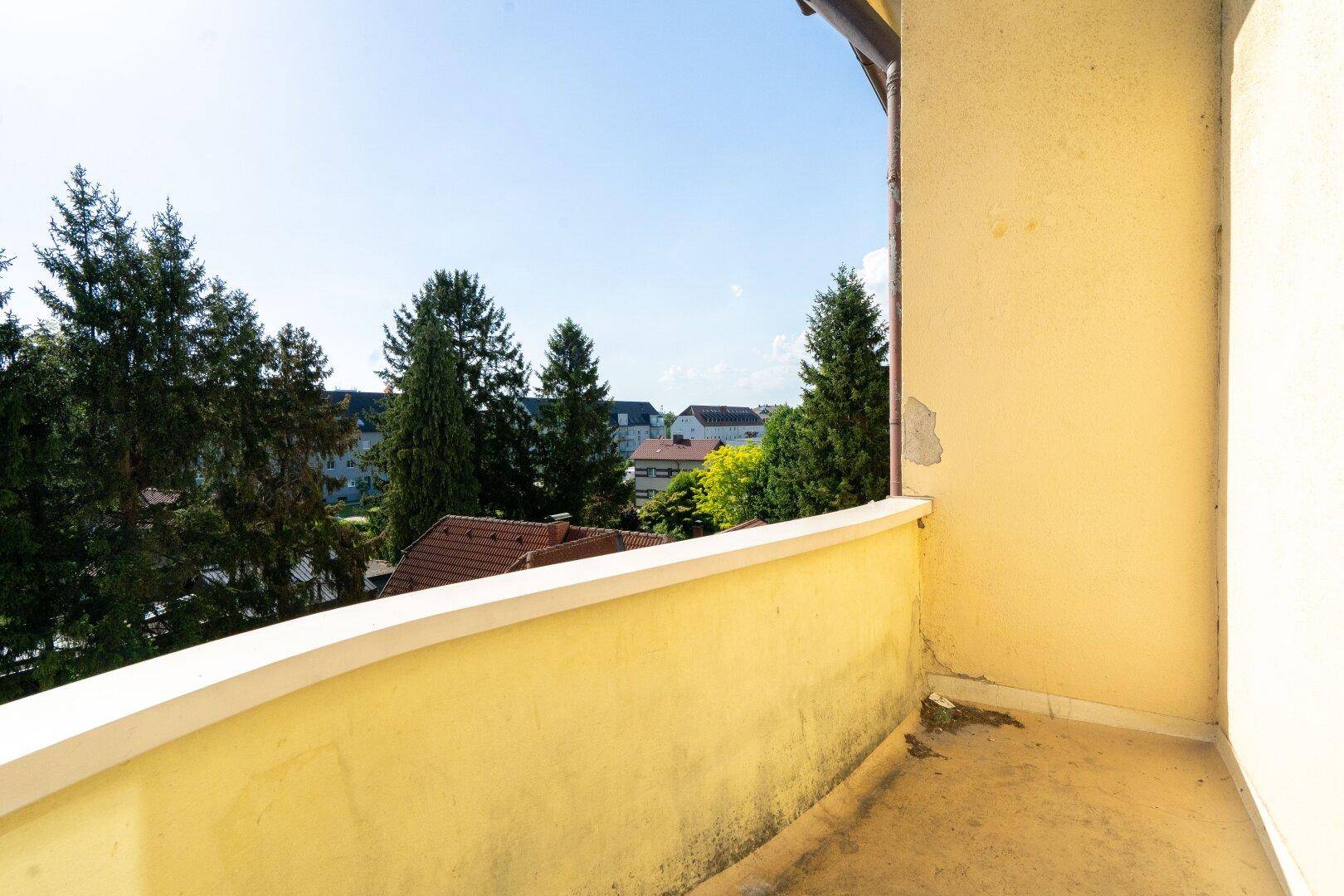 Kleiner Balkon mit gelber Brüstung und Blick auf Bäume und umliegende Häuser.