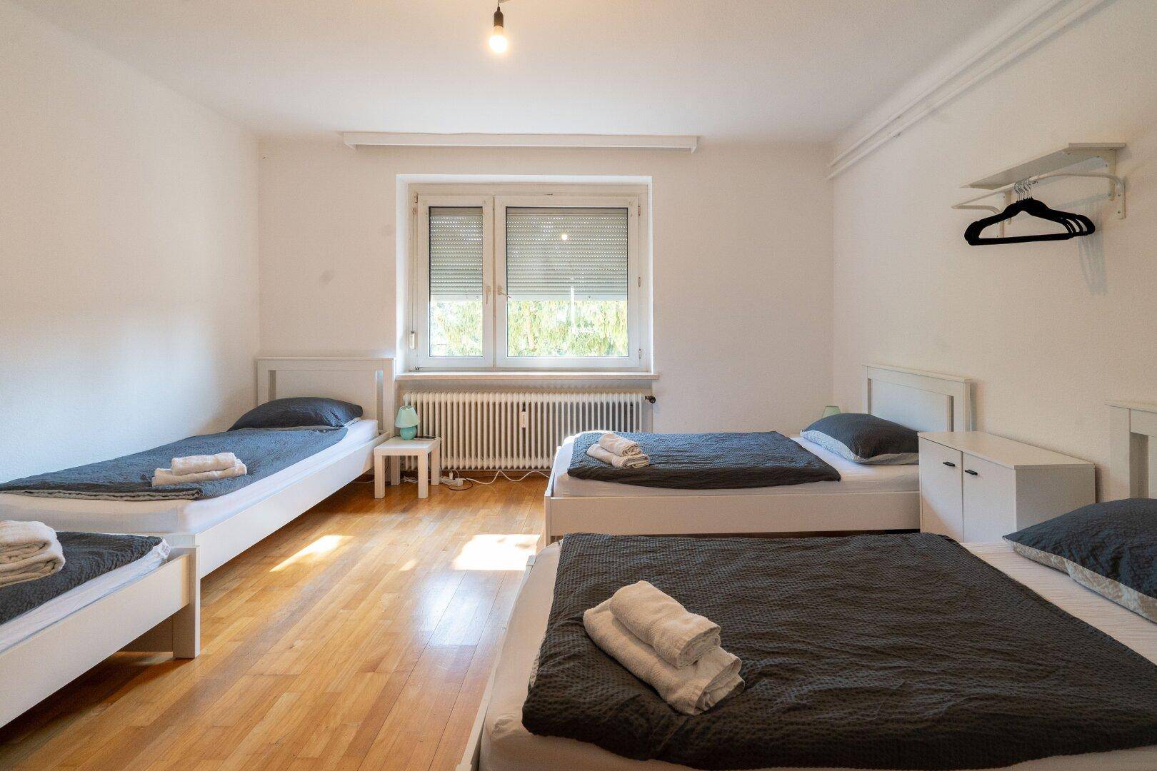 Geräumiges Schlafzimmer mit mehreren Einzelbetten, Holzfußboden und großen Fenstern.